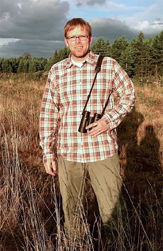 Man stands in field with binoculars. 