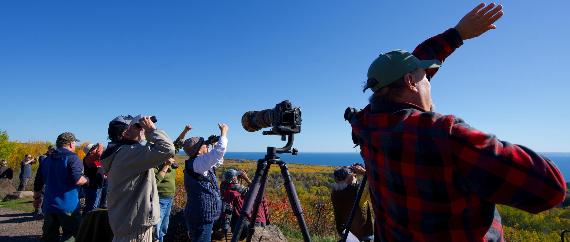 birdwatchers look at the sky during a hawk count with autumn colors and blue water in the distance